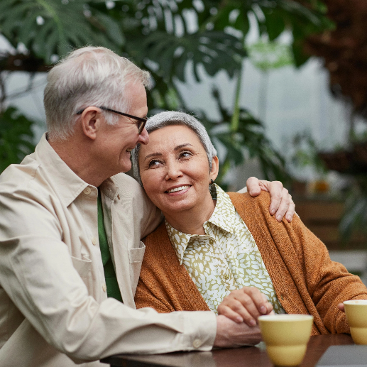 Older, retired couple sitting with cups of coffee and smiling at each other