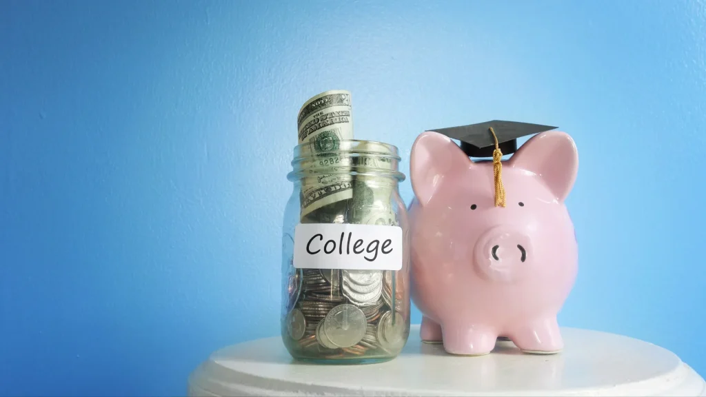 Piggy bank with graduation cap on sitting on table next to a jar of cash