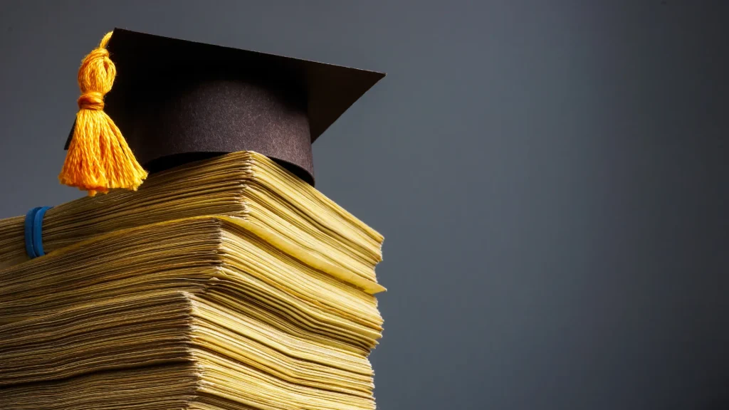 Stack of books and papers with a graduation cap sitting on top