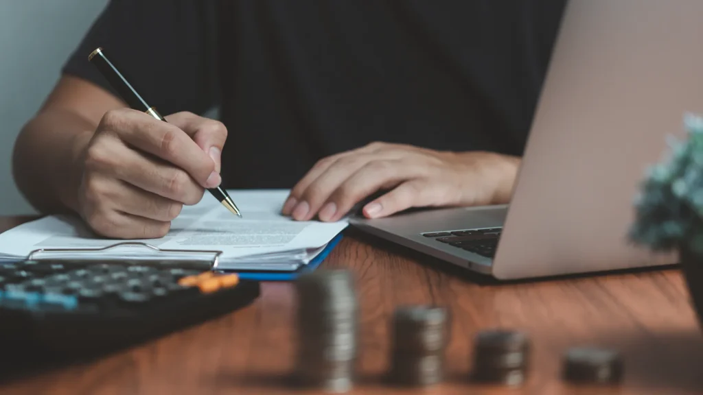 What Does SEP Stand For? - Man writing down information on paper with a calculator and laptop on desk