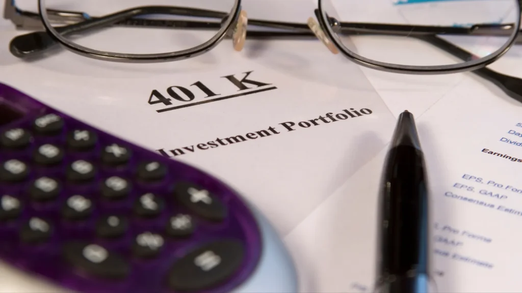 401(k) investment portfolio sitting on table with glasses, pen, and a calculator