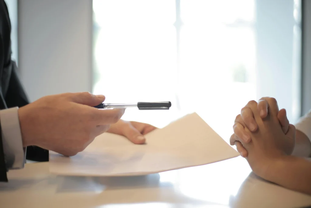 Financial planner holding out a paper and pen to client sitting with hands folded together