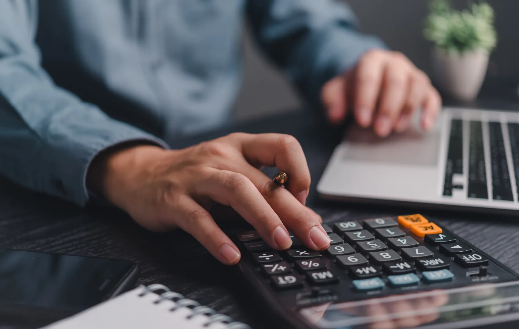 person typing numbers into calculator while learning how to create a budget